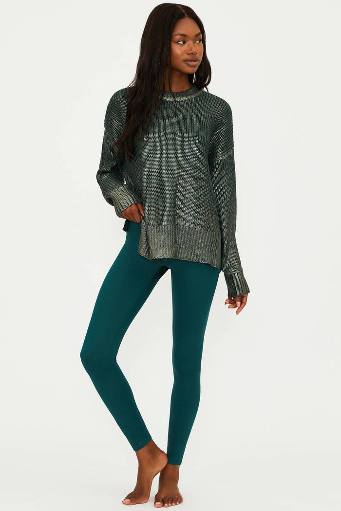 Woman wearing a dark green ribbed sweater and teal leggings on a white background