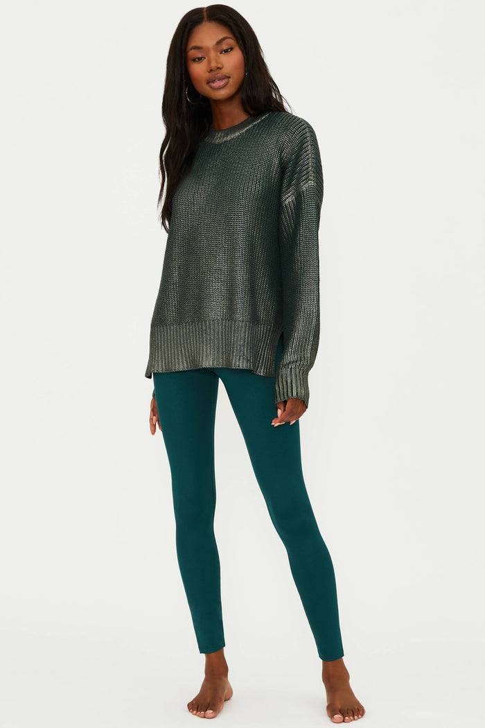 Woman wearing a dark green ribbed sweater and teal leggings on a white background