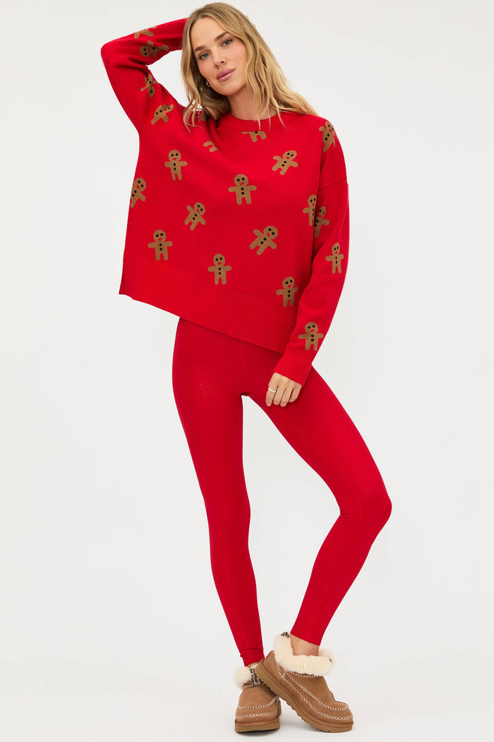 Woman wearing a red sweater and leggings with gingerbread men pattern on a white background
