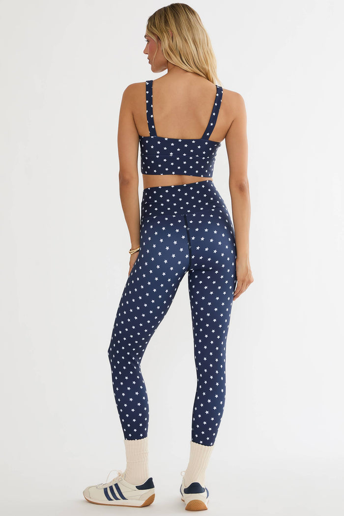 Woman wearing a navy blue polka dot sports bra and leggings set on a white background