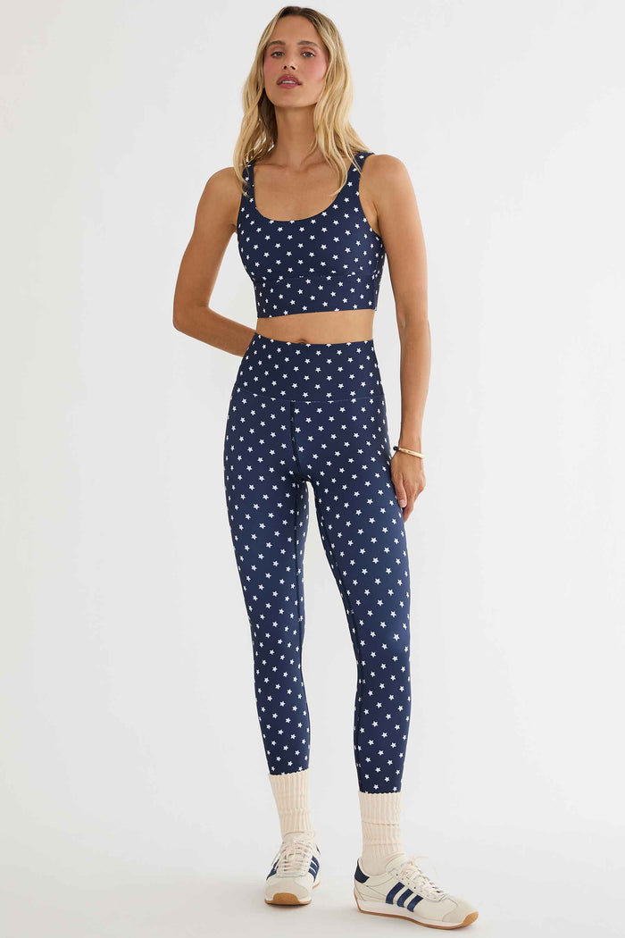 Woman wearing a navy blue sports bra and leggings with white polka dots on a white background
