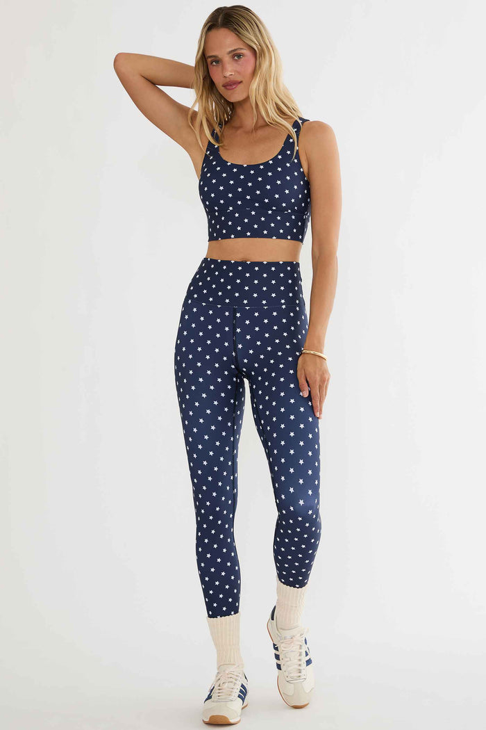 Woman wearing a navy blue sports bra and leggings with white star pattern on a white background