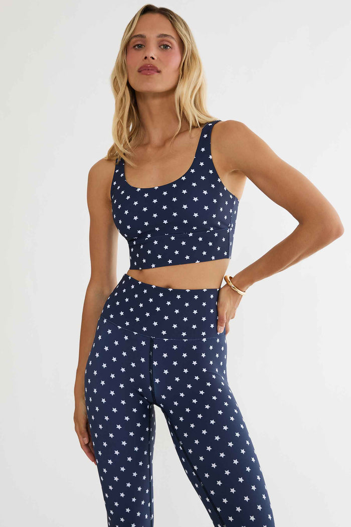Woman wearing a navy blue sports bra and leggings with white star patterns on a white background