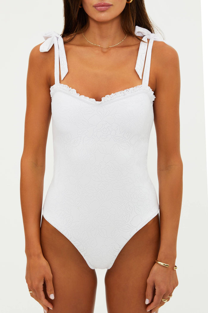 White swimsuit with bow straps worn by a model on a white background