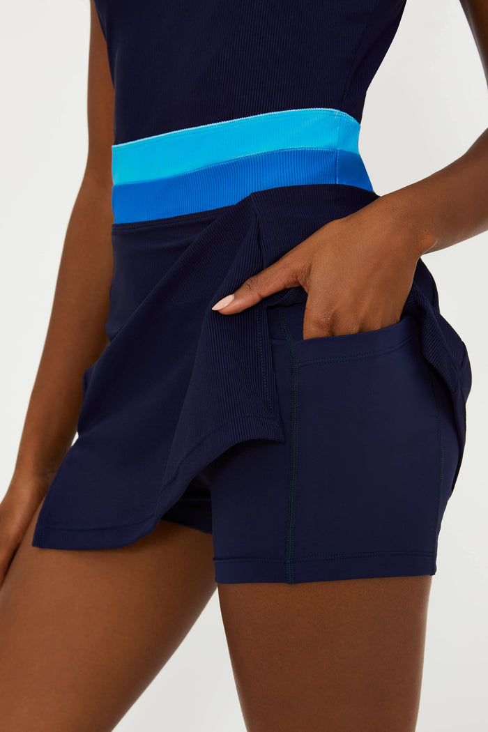 A model wearing a navy active dress with a bright blue colorblock stripe, featuring built-in shorts and a scoop neck.