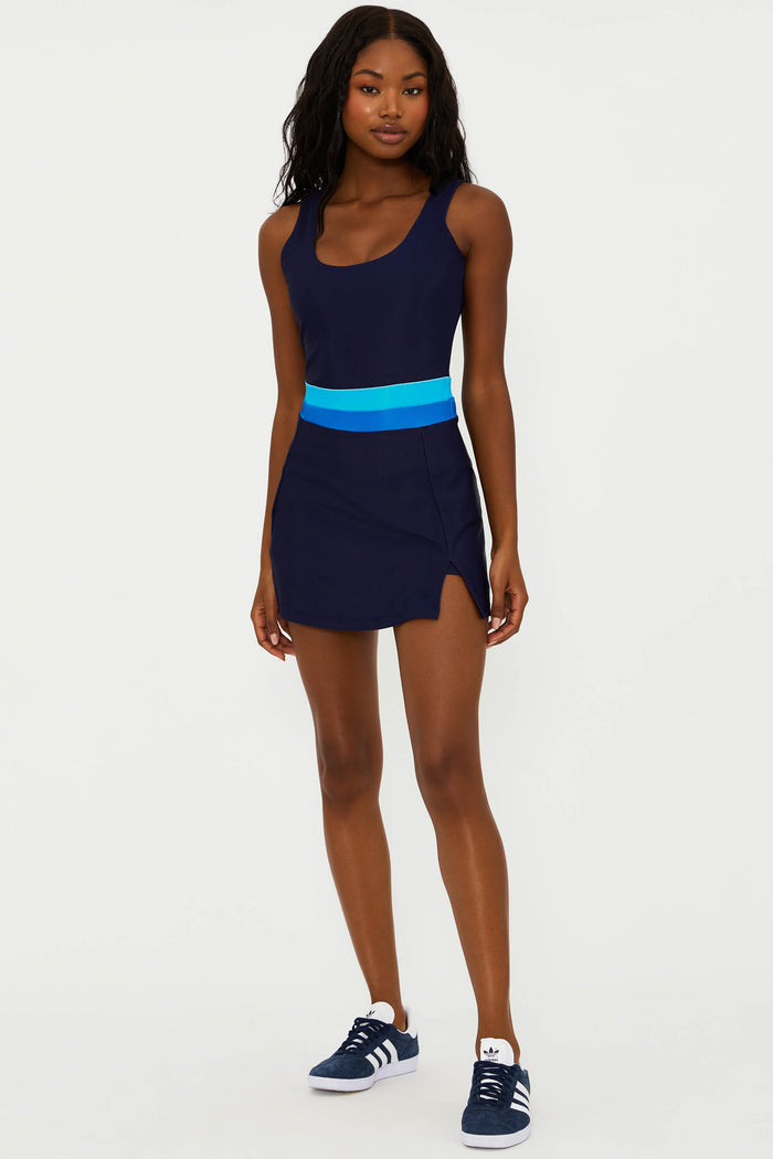 A model wearing a navy active dress with a bright blue colorblock stripe, featuring built-in shorts and a scoop neck.