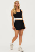 Model wearing a black active dress with white and tan colorblocking on the waistband, paired with white sneakers.
