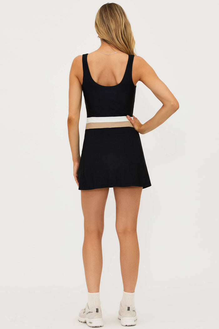 Model wearing a black active dress with white and tan colorblocking on the waistband, paired with white sneakers.