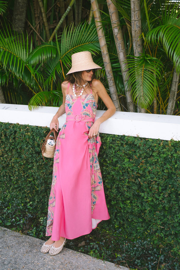 A woman modeling a bright pink maxi dress with intricate multicolor floral embroidery and a matching belt,