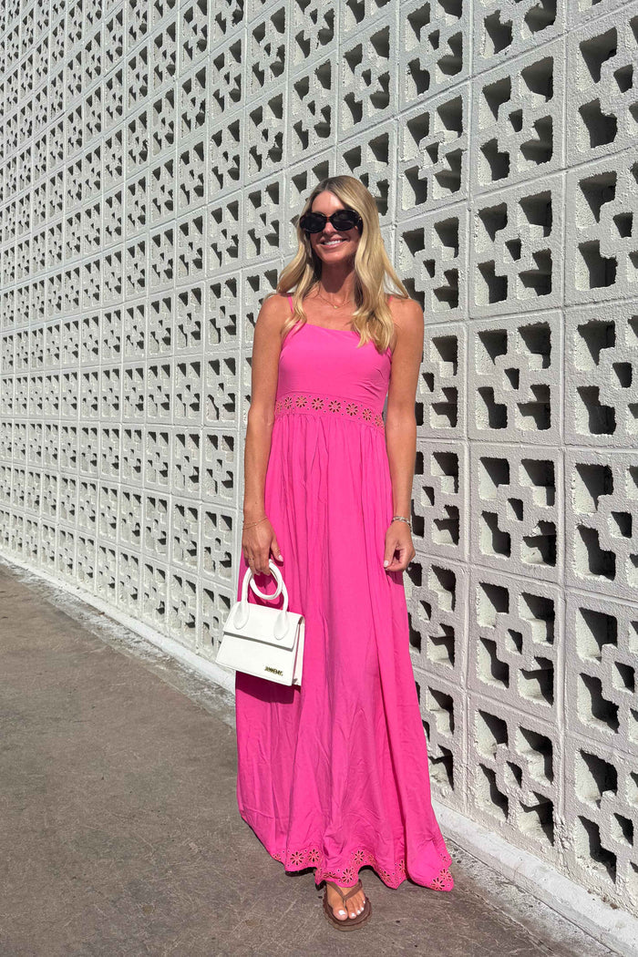 Woman in a pink dress standing against a textured wall.