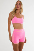 Woman wearing a pink sports bra and shorts set on a white background