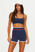 Woman wearing a navy sports bra and shorts with red accents on a white background