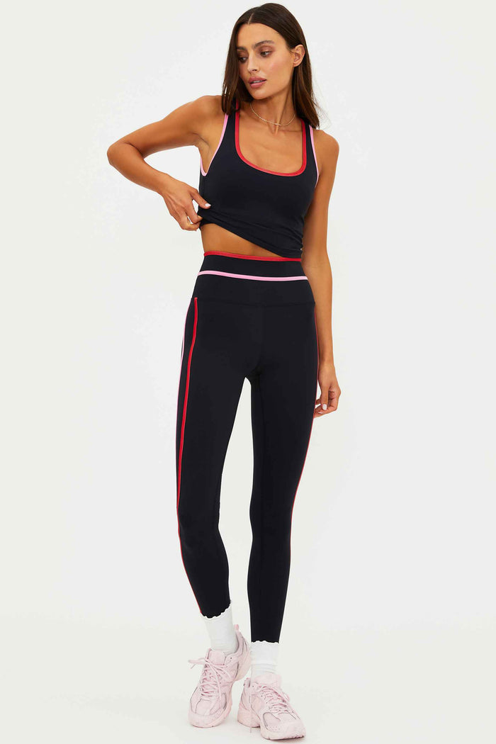 Woman wearing a black sports bra and leggings with pink accents on a white background