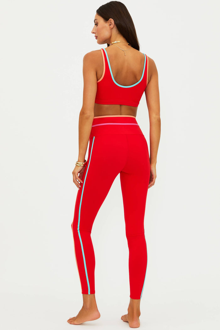 Woman wearing a red sports bra and leggings with white stripes on a white background