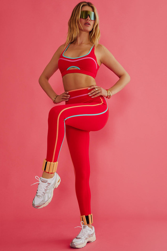 Woman in red athletic wear posing against a pink background