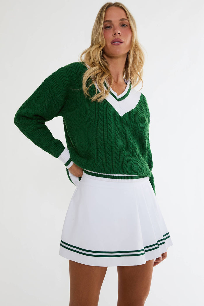 Woman wearing a green sweater and white skirt with green trim on a white background