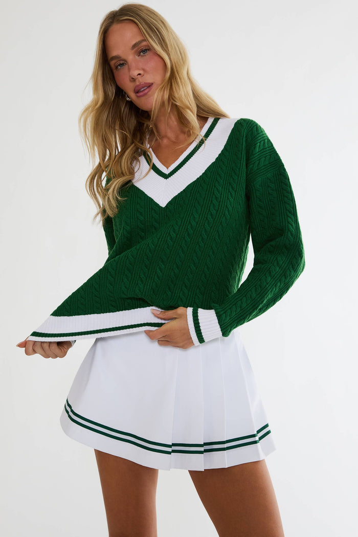 Woman wearing a green sweater with white trim and a white skirt with green stripes on a white background