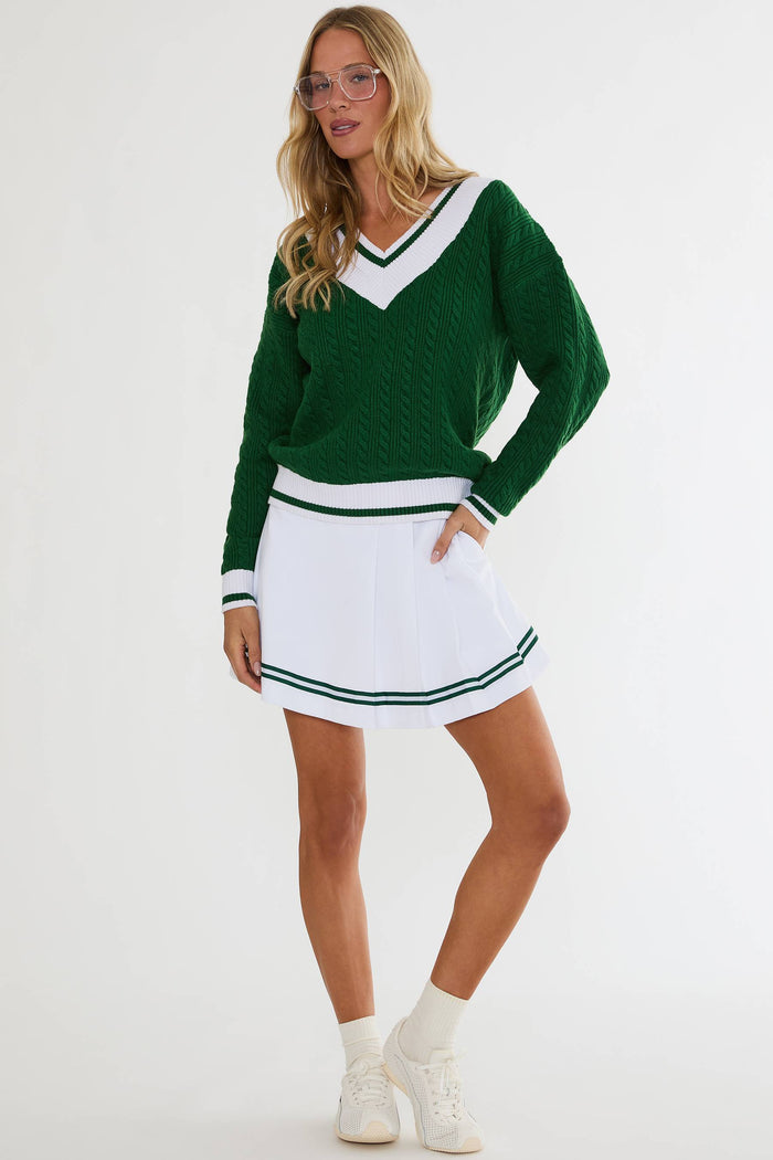 Woman wearing a green sweater and white skirt with green trim on a white background