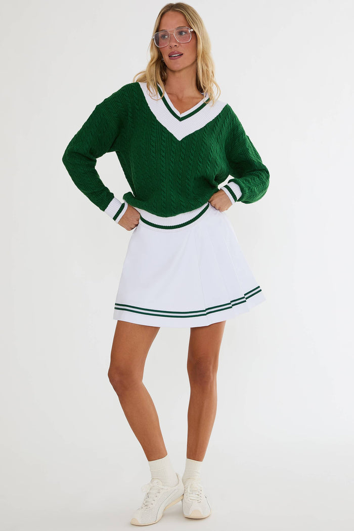 Person wearing a green sweater and white skirt with black trim on a white background