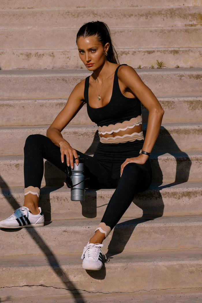 Woman in athletic wear sitting on stone steps holding a water bottle.