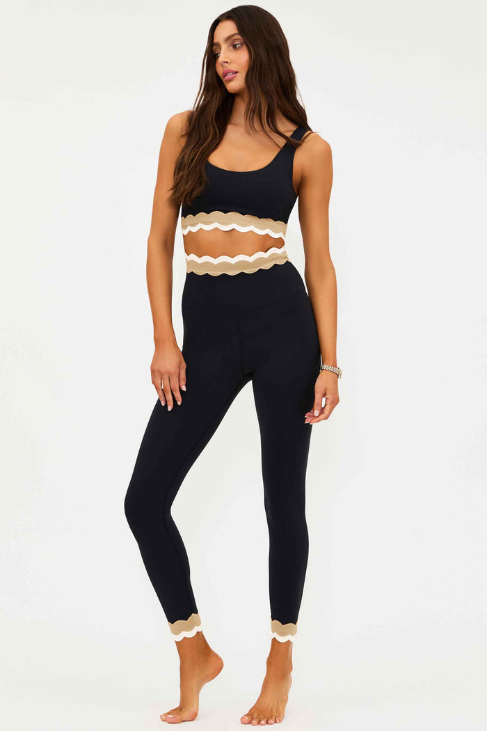 Woman wearing a black and beige sports bra and leggings set on a white background