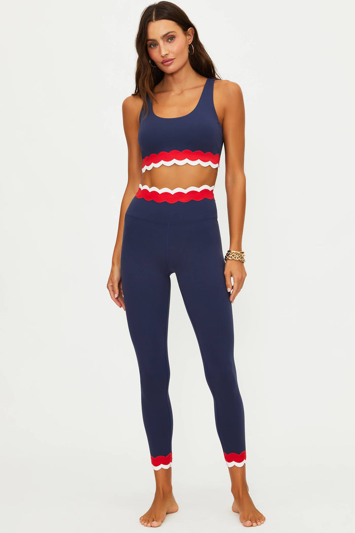 Woman wearing a navy blue sports bra and leggings with red accents on a white background