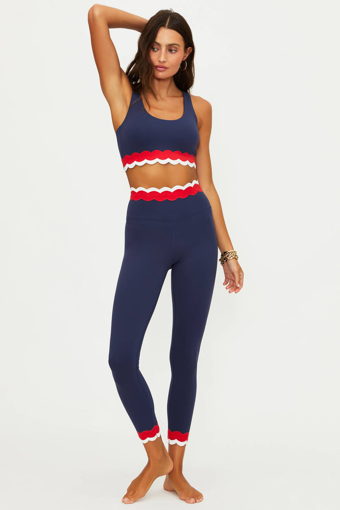 Woman wearing a navy blue athletic outfit with red accents on a white background