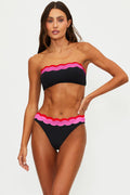 Woman wearing a black and pink bikini with scalloped edges on a white background
