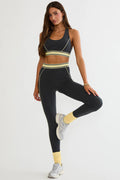 Woman wearing a black sports bra and leggings with yellow accents on a white background