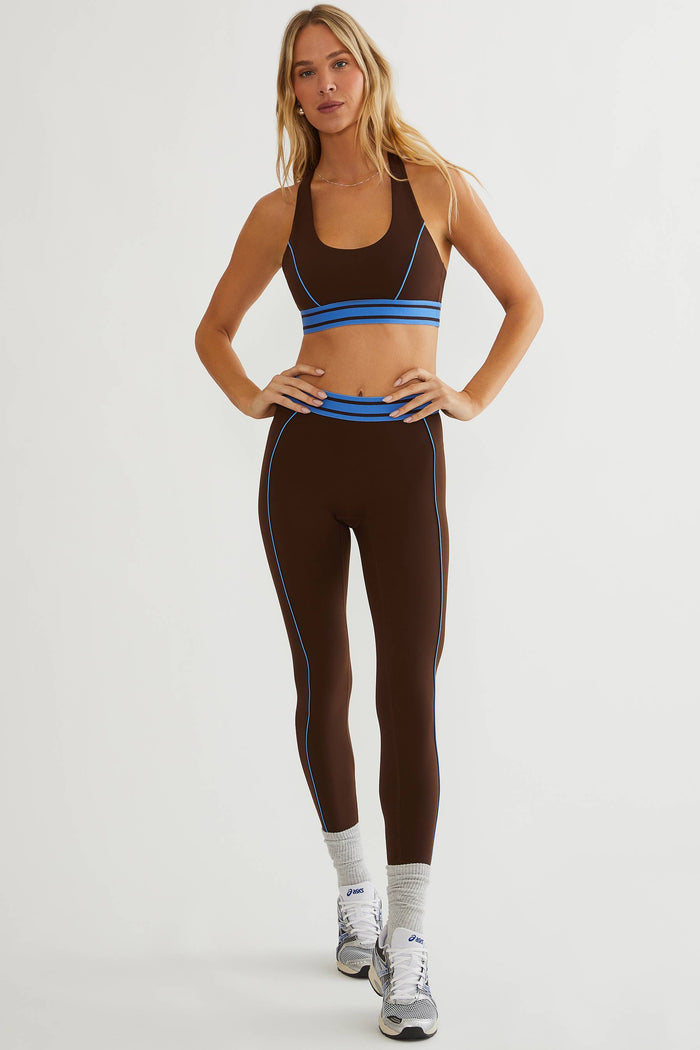 Woman wearing brown leggings with blue detailing on a plain white background.