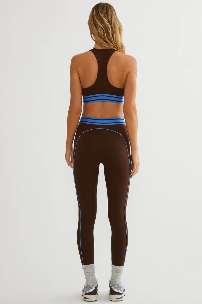 Woman wearing brown leggings with blue detailing on a plain white background.