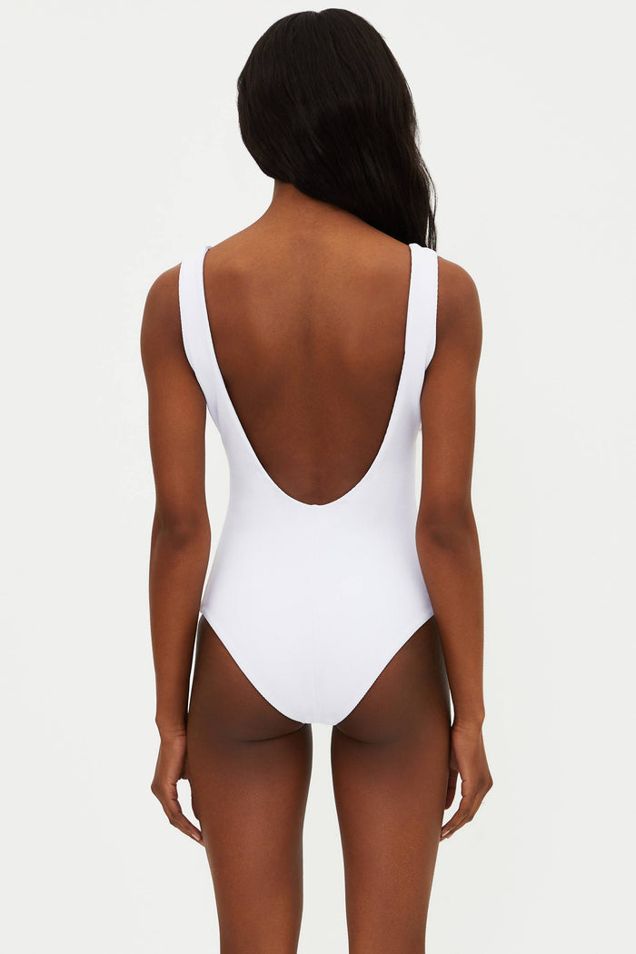 A model is wearing a white one-piece swimsuit with a ribbed texture, fixed straps, and a low back.