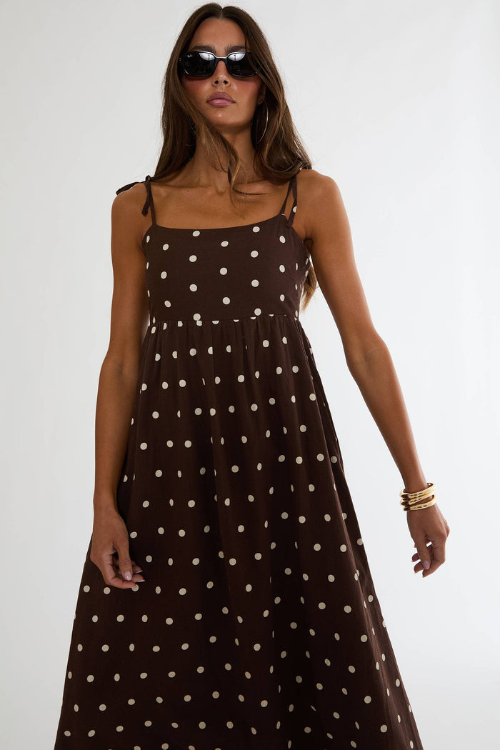 Woman wearing a brown polka dot dress with sunglasses on a white background