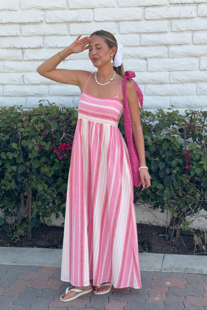 Woman in a pink and white striped dress standing against a white brick wall with greenery.