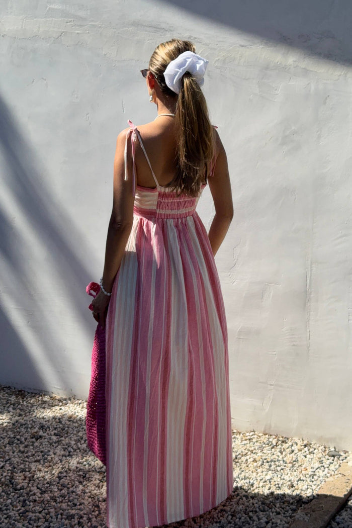 Woman wearing a pink and white striped dress against a light gray wall.