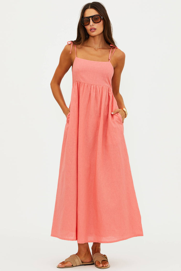 Woman wearing a coral pink dress with thin straps on a white background