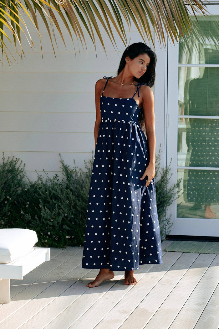 A navy maxi dress with white polka dots, featuring tie shoulder straps and side pockets.
