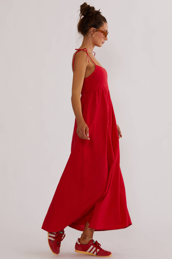 A model wearing a red maxi dress with tie shoulder straps and side pockets.
