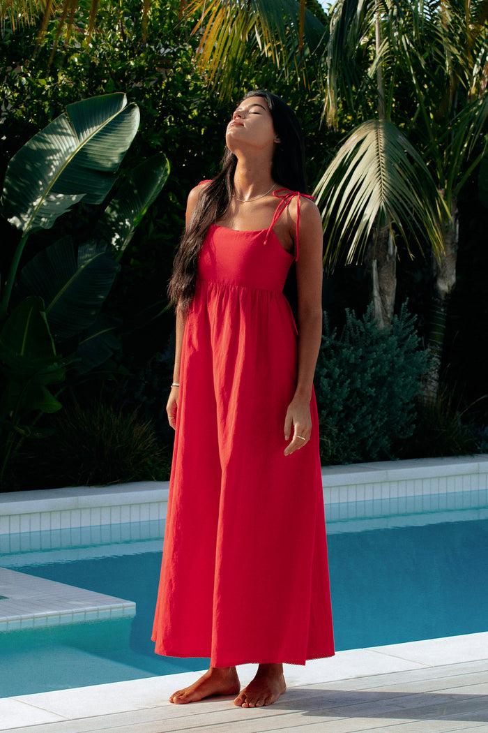 A model wearing a red maxi dress with tie shoulder straps and side pockets.