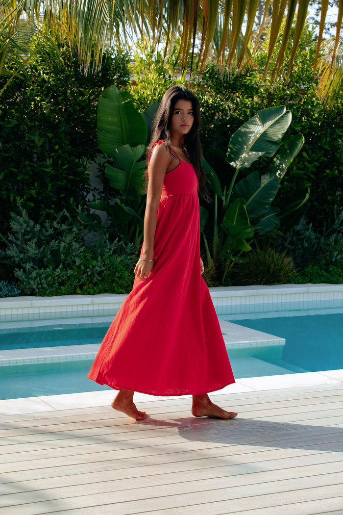 A model wearing a red maxi dress with tie shoulder straps and side pockets.
