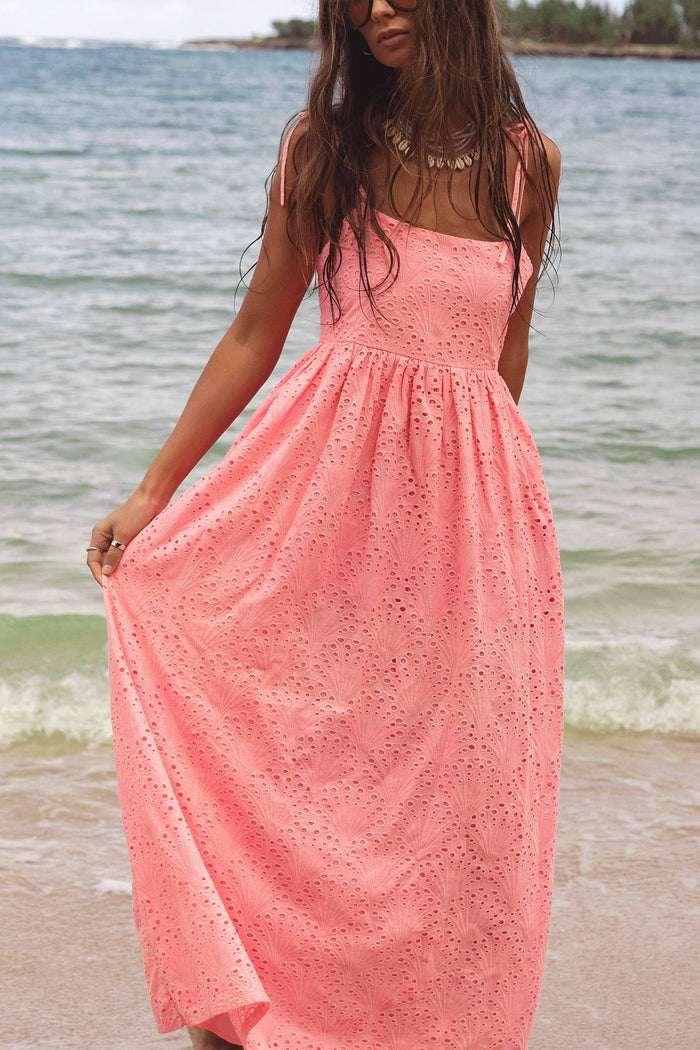 Woman in a pink dress standing on a beach with water in the background