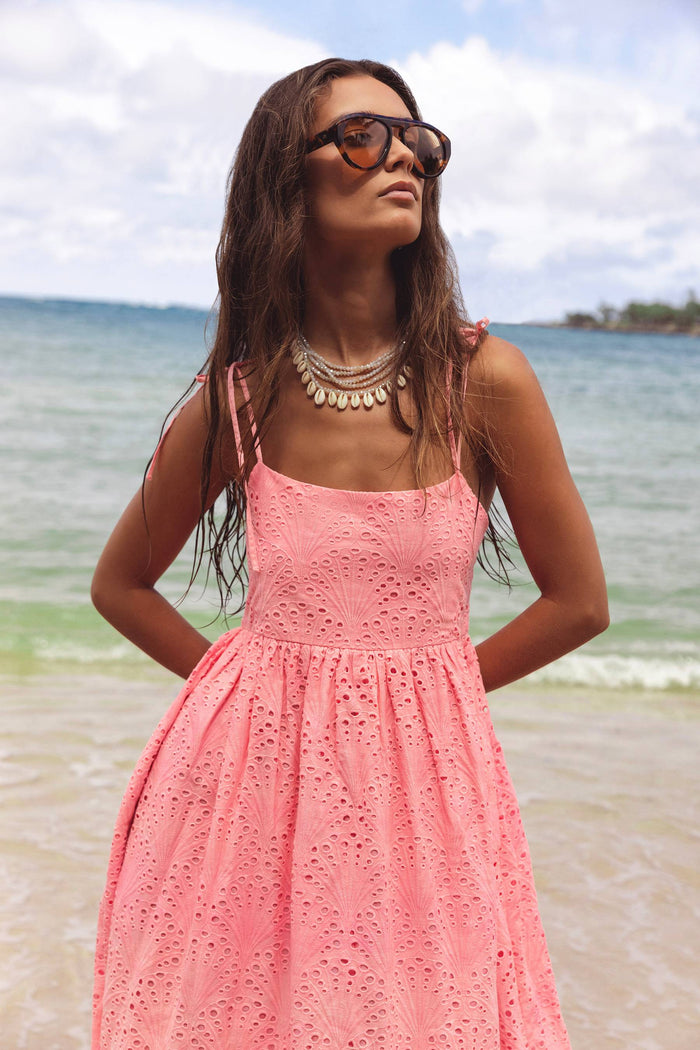 Woman in a pink dress standing on a beach with ocean and sky in the background