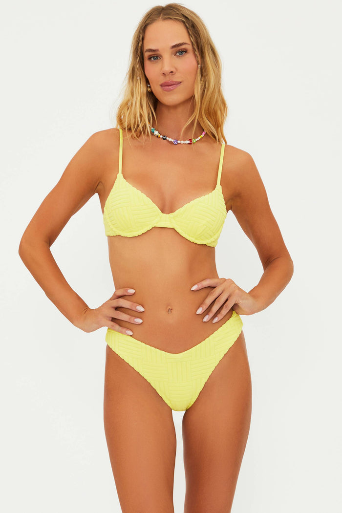 A model wearing a yellow underwire bralette style swim top with adjustable straps and a matching bottom, accessorized with a necklace.