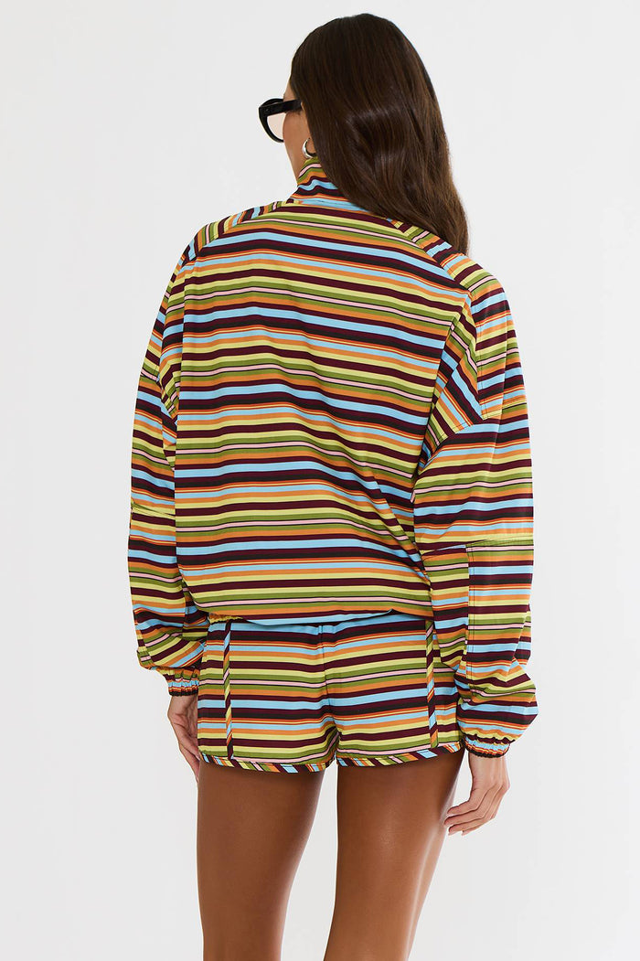 A woman shown from the back wearing a long-sleeve collared top and matching shorts with horizontal multicolor stripes in yellow, blue, brown, orange, and white, against a plain light gray studio background.
