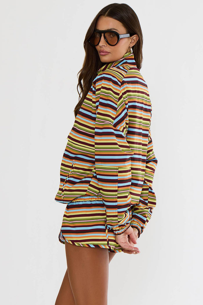 A woman modeling a matching striped long-sleeve top and shorts set against a plain white studio background. The set features horizontal stripes in yellow, orange, brown, blue, and white.