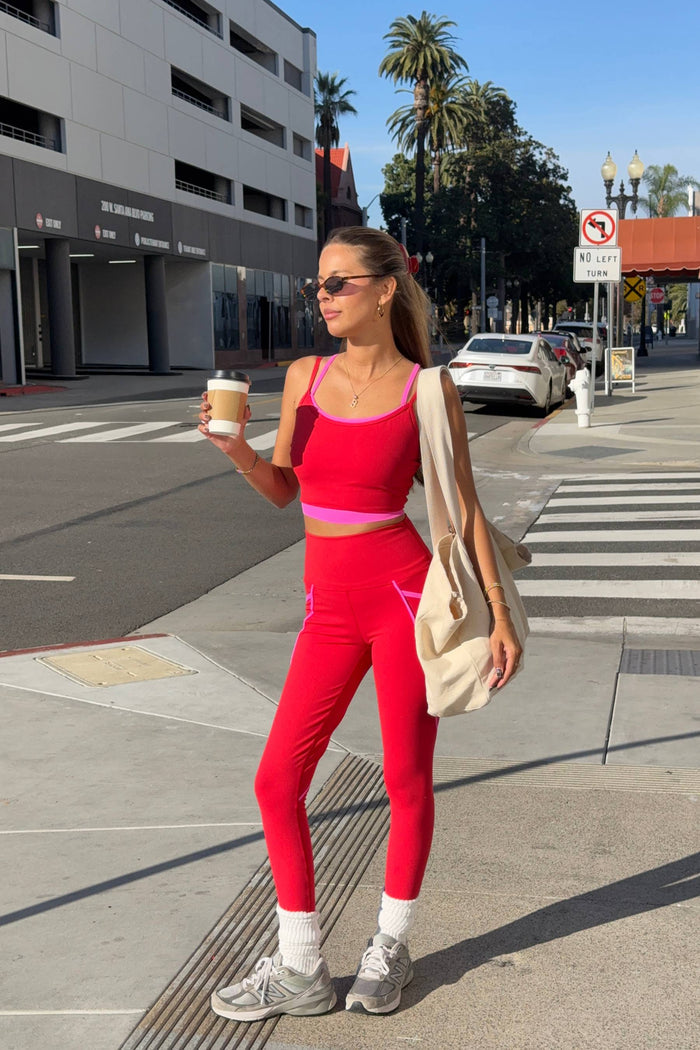 Woman in red athletic wear holding a coffee cup on a city street.