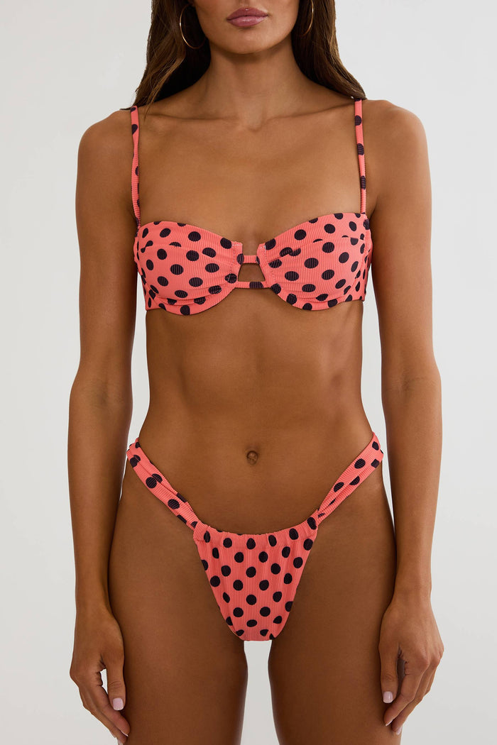 Woman wearing a pink bikini with black polka dots against a white background