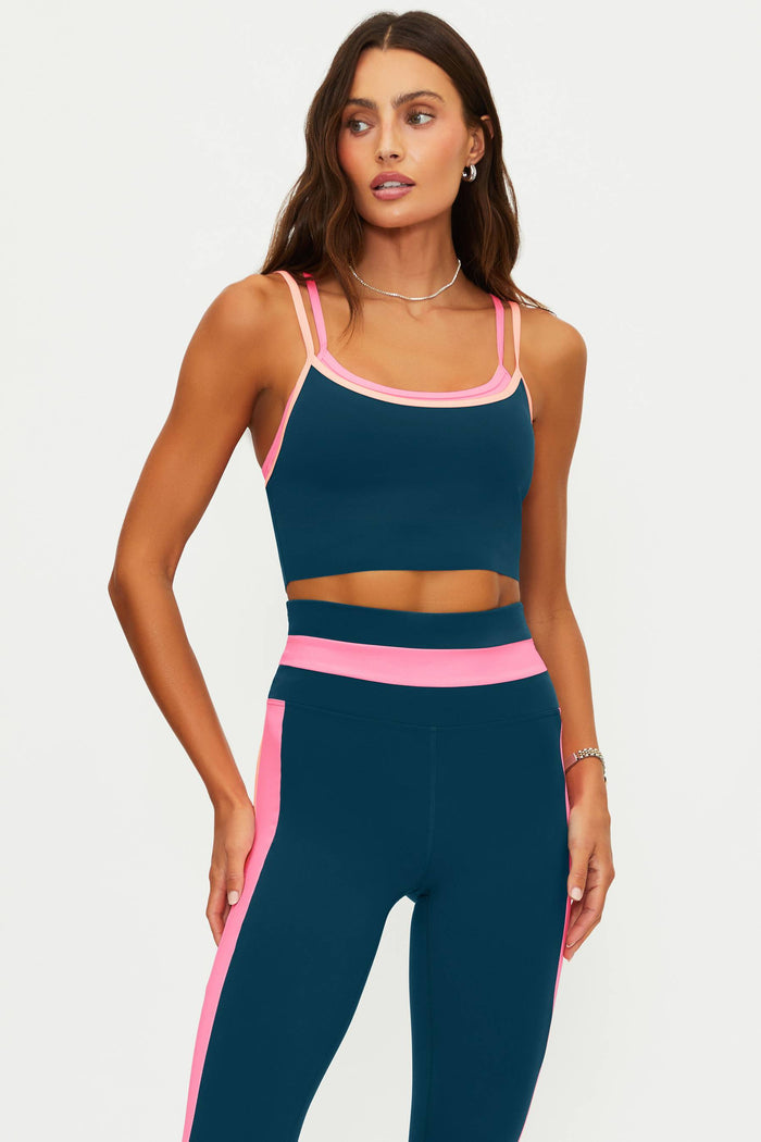 Woman wearing a navy sports bra and leggings with pink accents on a light gray background