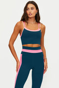 Woman wearing a navy sports bra and leggings with pink accents on a light gray background