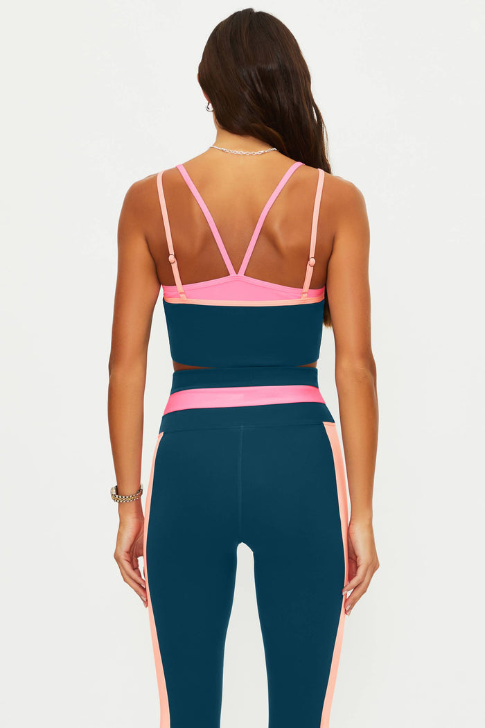 Woman wearing a teal and pink sports bra and leggings set on a white background